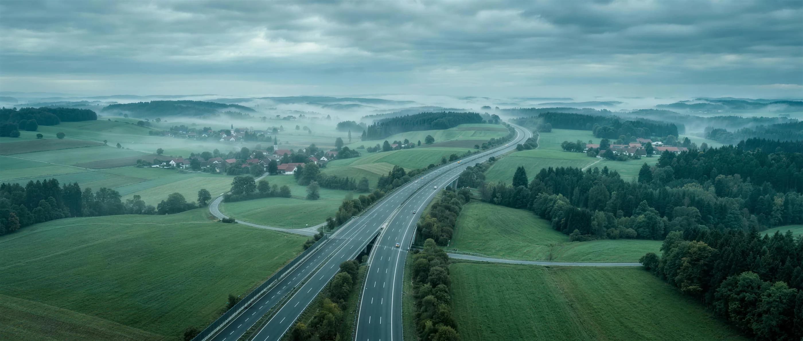 Luftbild einer Autobahn, die sich an einem nebligen Morgen durch grünes Land zieht