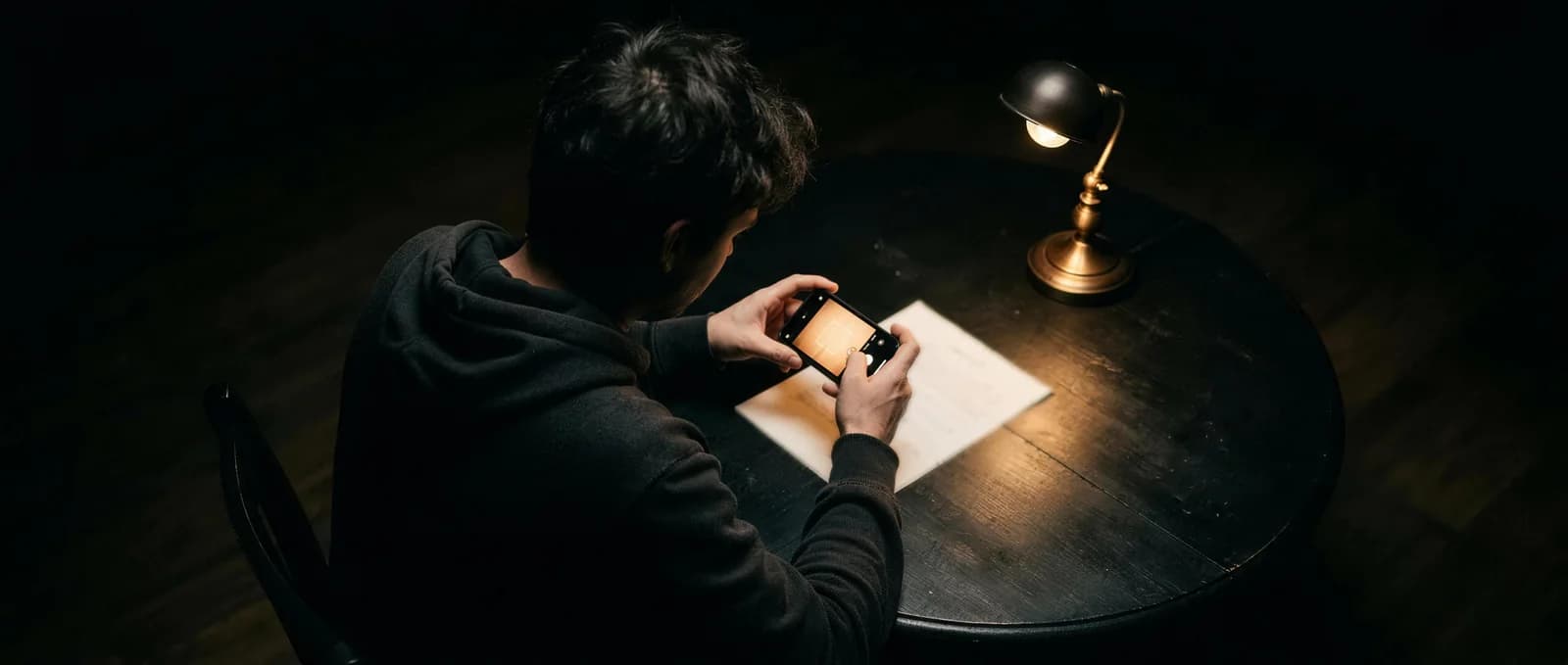 Eine Person fotografiert am Abend am Tisch ein Dokument mit dem Smartphone ab
