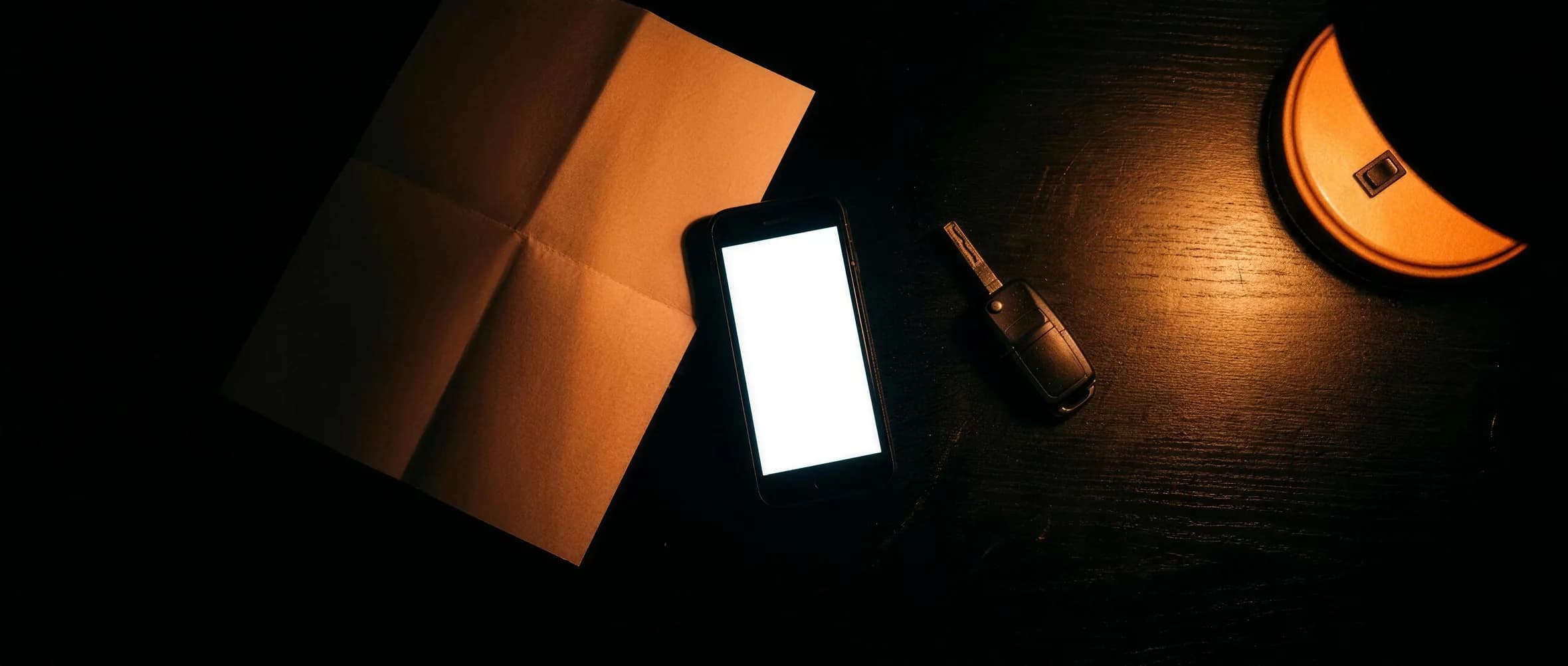 Fahrzeugpapiere, ein Autoschlüssel und ein Smartphone auf einem dunklen Tisch unter einer Lampe