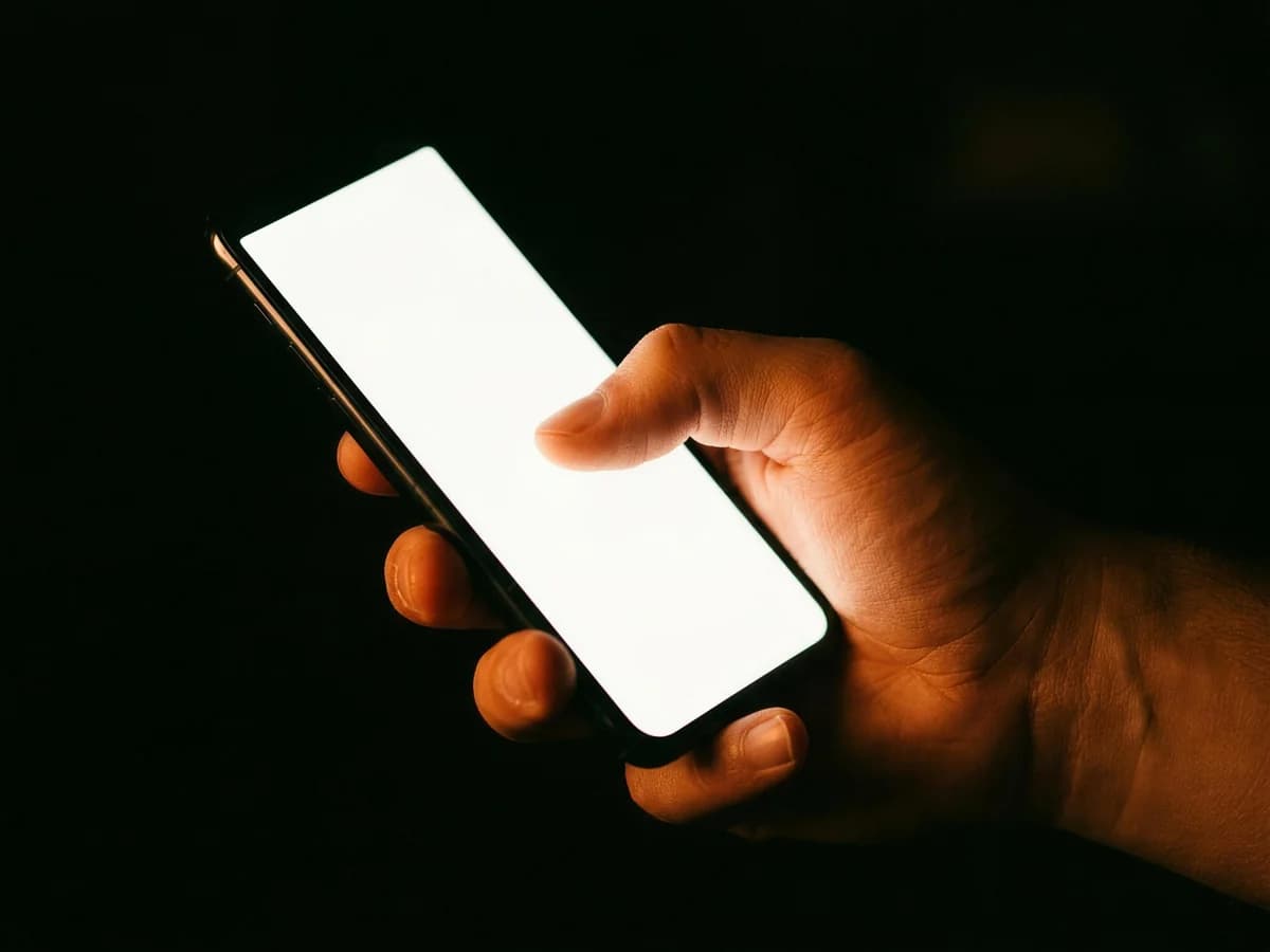 Eine Hand hält im Dunkeln ein Smartphone, ein Finger unterschreibt auf dem leuchtenden Display